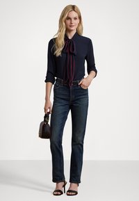 Bluză bleumarin cu o cravată roșie, croi ajustat; purtată cu blugi de denim închisi și sandale negre cu curele. Geantă mică cu accesorii aurii.