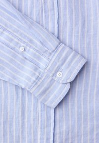 Chemise bleu clair à manches longues avec des rayures blanches verticales, poignet boutonné et boutons blancs assortis sur la patte de manche.