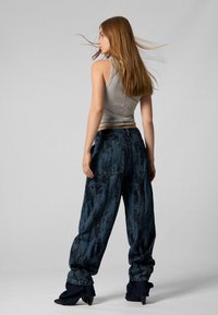 Hallitusseente pitsiga hall sobiv tank top ja laiad tumesinised teksapüksid tekstuuriga mustriga. Mudel kannab siniseid rulluisu saapaid.