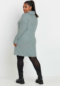 Ljust grå hoodie-klänning med långa ärmar, ribbade detaljer och rak skärning, i kombination med svarta tights och grova svarta stövlar.