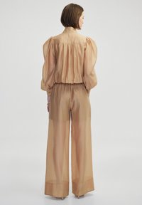 Beige doorschijnende twee-delige outfit met een top met pofmouwen en een geplooide achterkant, en brede broek met een elastische tailleband.