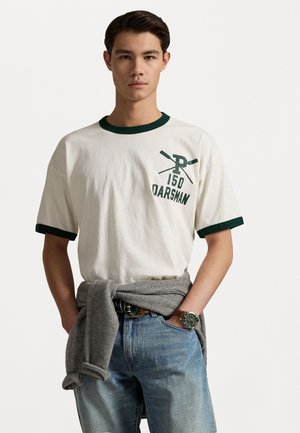 White cotton t-shirt with green ribbed collar and cuffs, featuring the text "150 OARSMAN" and crossed oars graphic. Accompanied by grey sweater tied at waist.