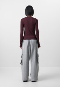 Långärmad bordeauxfärgad topp och grå vida mjukisbyxor med cargofickor. Tyget verkar mjukt; byxorna har en avslappnad passform och dragsko i midjan.