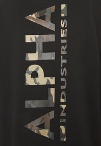 Sudadera negra con texto vertical grande "ALPHA" en un patrón de camuflaje y "INDUSTRIES" en blanco sólido. Textura suave, estilo casual.