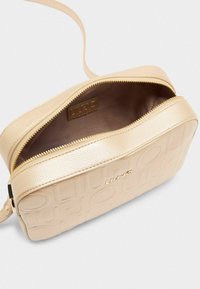 Geantă din piele bej tip crossbody cu logo embosat, finisaj texturat, închidere cu fermoar și curea detașabilă. Interior căptușit vizibil.