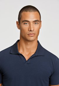 Polo de color azul marino hecho de una suave mezcla de algodón, con un clásico cuello, mangas cortas y un corte relajado. Sin patrones visibles.