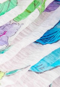 Gros plan sur un tissu blanc texturé avec des motifs floraux colorés en tons verts, violets, bleus et roses.