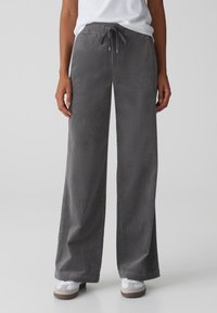 Pantalon en velours côtelé gris à coupe ample, doté d'une taille à cordon de serrage et de jambes larges. Texture côtelée subtile qui ajoute de la profondeur; associé à des baskets blanches.