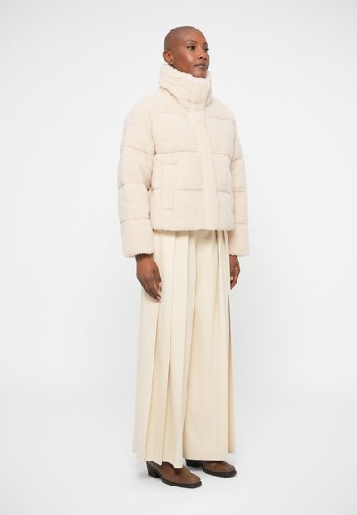 Off-white quilted puffer jacket with high collar, featuring a soft texture and side pockets, paired with wide cream trousers.