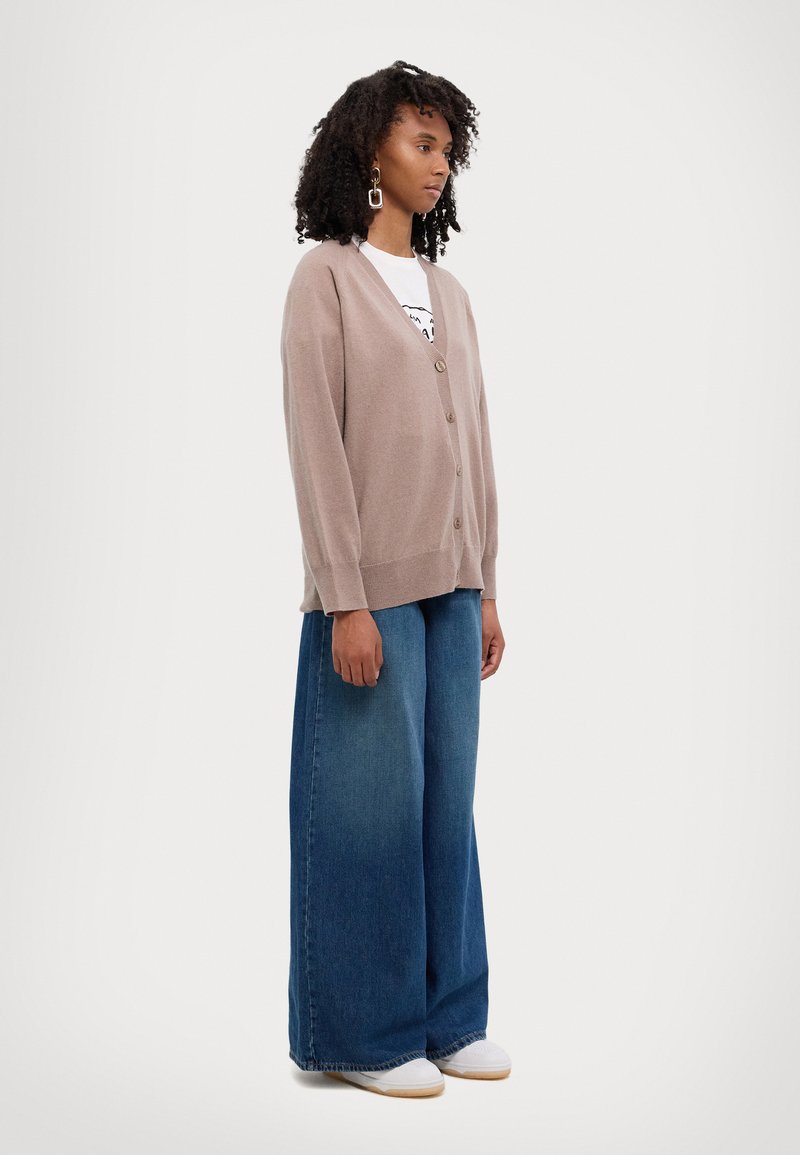 Light brown cardigan with a v-neck, button closure, and long sleeves, paired with wide-leg blue denim pants and white sneakers.