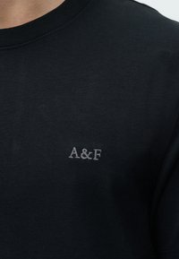 Черен тениска с малко сиво бродирано лого "A&F" в областта на лявата част на гърдите и рипсен кръгъл деколте.