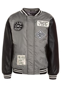 Šedá bomber bunda s černými koženými rukávy, která má několik nášivek a pruhované manžety. Materiály zahrnují hladkou tkaninu a kůži.