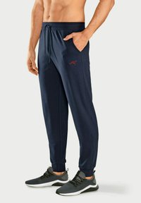 Herren Jogginghosen in Marineblau mit elastischem Bund und Kordelzug, seitlichen Taschen, schmalem Schnitt und einem kleinen roten Logo am linken Oberschenkel.