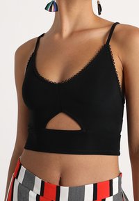 Top court noir avec encolure en V, présentant des bords festonnés et un design découpé. Tissu doux et extensible qui souligne une silhouette ajustée.