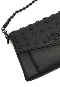 Svart clutch i fusk läder med en texturerad yta, prydd med mattsvarta dekorativa nitar, ett lockstängning och en flätad kedjesladd.