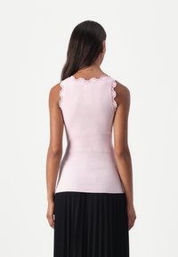 Débardeur en ribbed rose clair avec une bordure en dentelle sur les épaules, au design ajusté, porté avec une jupe plissée noire, vu de dos.