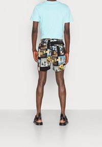 Un t-shirt bleu clair à manches courtes associé à un short noir à motifs présentant des photos et des accents jaunes. Des sandales complètent la tenue.