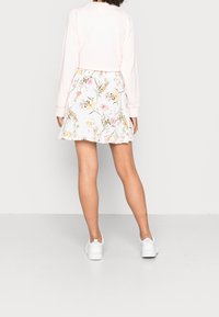 Haut rose à manches longues associé à une jupe blanche à fleurs avec des imprimés botaniques multicolores, taille élastique et coupe évasée.