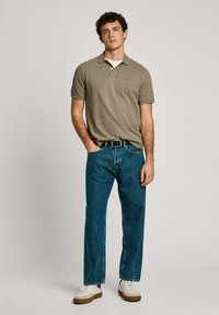 Polo skjorte i olivengrøn med korte ærmer, parret med blå denim jeans og hvide sneakers med brune såler. Bælte i taljen.