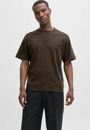 Camiseta de algodón marrón con mangas cortas, cuello redondo y corte relajado. Se lleva con pantalones oscuros. Tejido texturizado. Diseño simple, sin patrones.