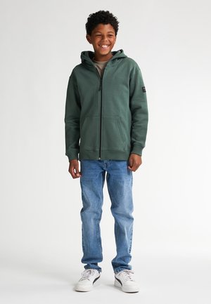 Groene ritshoodie met een voorzak en verstelbare capuchon, in combinatie met lichtblauwe jeans en witte sneakers. Eenvoudig ontwerp en zachte textuur.