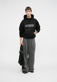 Melna pārāk liela kapuce ar "wastedparis" grafiku, apvienota ar brīviem pelēkiem biksēm un melnām kurpēm, turētā melna iepirkumu soma. Gludas auduma tekstūras.