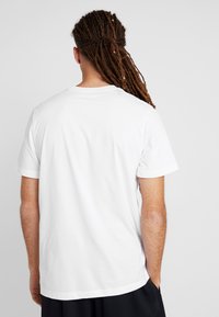 Camiseta de algodón blanca con mangas cortas y un escote redondo. La parte trasera presenta una superficie lisa y texturizada, y tiene un ajuste relajado.