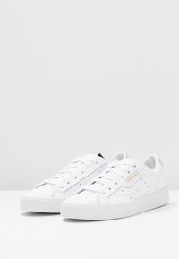 Vita låga sneakers i slätt läder med ett perforerat mönster. Har vita snören och en subtil beige accent vid hälen.