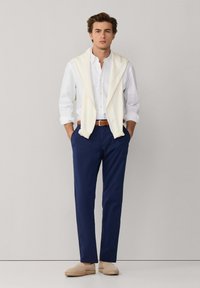 Camicia bianca con bottoni, maglione crema drappeggiato sulle spalle, pantaloni blu navy e espadrillas beige. Design semplice con un aspetto rilassato.