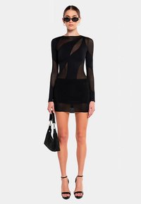 Sort langærmet kjole med gennemsigtige paneler og tekstureret nederdel. Bær med sorte solbriller og en lille håndtaske, kombineret med høje hæle.