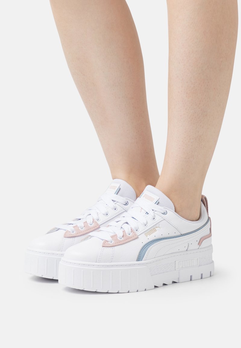 Zapatillas de plataforma blancas con un acabado de cuero suave, acentos en rosa y azul pastel, cordones planos y una suela de goma texturizada.