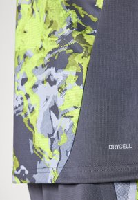 Kortærmet sportstrøje i grå med levende grøn og grå abstrakt mønster. Har struktureret stof og "DRYCELL" branding på kanten.