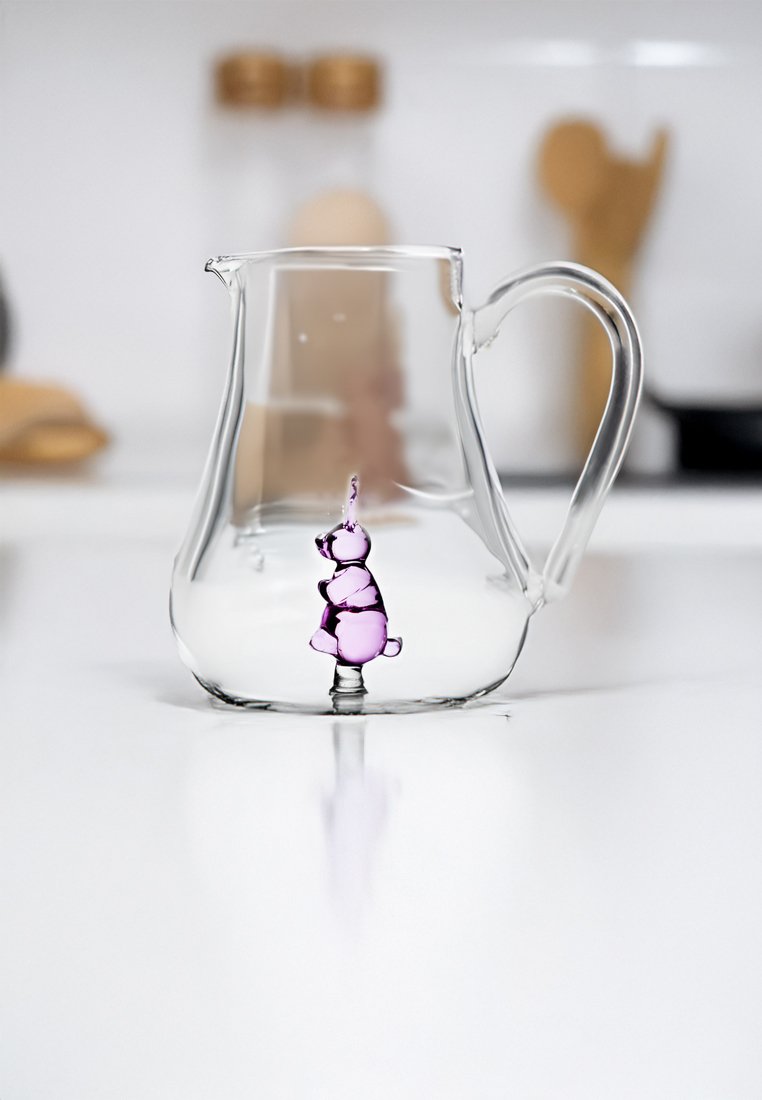 Przezroczysty szklany dzbanek z zaokrąglonym korpusem i uchwytem, wypełniony płynem o kształcie fioletowego misia, ustawiony na białej powierzchni.