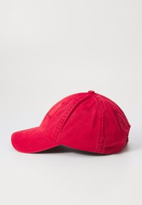 Red cotton baseball cap with a curved brim; features stitched ventilation holes and a fabric strap at the back for adjustment.