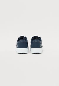 Chaussures de sport bleu marine avec une tige synthétique lisse, une semelle intermédiaire blanche rembourrée et une semelle extérieure en caoutchouc noir dotée de petites pointes d'adhérence.