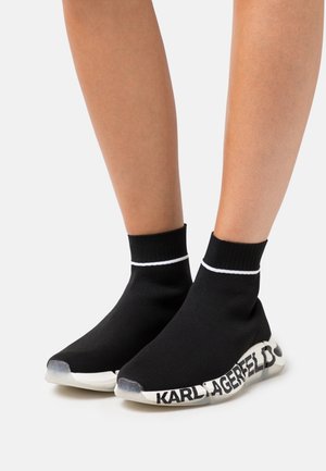 Sneakers calzini neri in maglia con banda alla caviglia a righe bianche, caratterizzate da una suola in gomma bianca con la scritta "KARL LAGERFELD" lungo il lato.