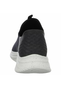 Zwarte instap sportieve schoen met een gestructureerde stoffen bovenkant, elastische zijkanten en een wit gespikkelde rubberen zool.