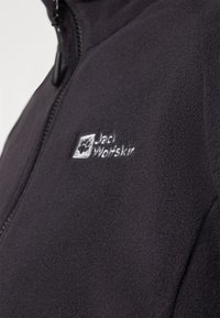 Black fleece jacket with a zip closure, featuring a textured fabric and embroidered logo on the chest. Simple, functional design.