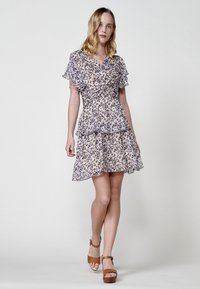 Kurzes Blumenkleid aus leichtem Stoff, mit Rüschensäumen, einem V-Ausschnitt und einem geschichteten Design in neutralen Farben mit dunklen Punkten.