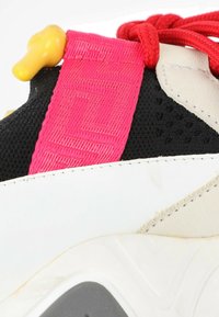 Gros plan d'une basket avec un mesh noir, du cuir blanc, une languette en tissu rose vif, des lacets rouges et un verrou en plastique jaune pour les lacets.