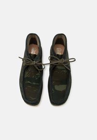 Skor med kamouflagemönster, mörkgrön tygovandel, beige läderfoder och bruna snören. Gummisula, rund tå.