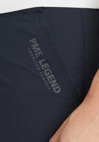Marineblauwe shorts met een gladde textuur, voorzien van het "PME LEGEND" logo in grijs. Details zijn fijne stiksels langs de randen.