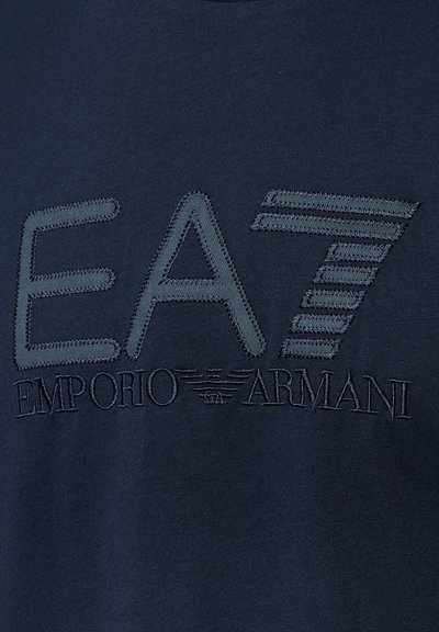 Donker marineblauw stof met een gestikte EA7 Emporio Armani logo waarin grote letters zijn verwerkt en een gestreept nummer zeven.
