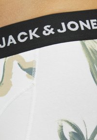 Weiße Boxershorts mit grün-beigem Blumenmuster, ausgestattet mit einem schwarzen elastischen Bund mit der Aufschrift "JACK & JONES" in weißer Schrift.