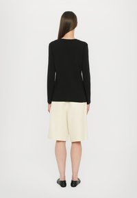 Long-sleeve black top paired with cream-colored shorts. The top has a round neckline; shorts feature a loose fit and soft texture.