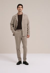 Traje gris claro texturizado con blazer de un solo botón y pantalones de corte plano, combinado con una camiseta marrón oscuro y calzado negro.