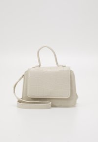 Beżowa torebka w wzór krokodyla z górnym uchwytem i odczepianym paskiem na ramię. Posiada zapięcie na klapkę oraz usztywniony kształt.