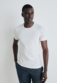 T-shirt blanc à manches courtes avec un col rond, texture lisse et design ajusté, associé à un pantalon noir à rayures.