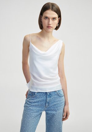Witte camisole met kraag en dunne bandschouderbandjes, gladde stof, zachte glans, gelaagde zoom, gecombineerd met lichtblauwe denim jeans met stippen.