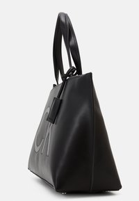 Sac à main en cuir noir de forme triangulaire, dotée d'une texture lisse, de deux poignées sur le dessus et d'un grand logo en relief à l'avant.